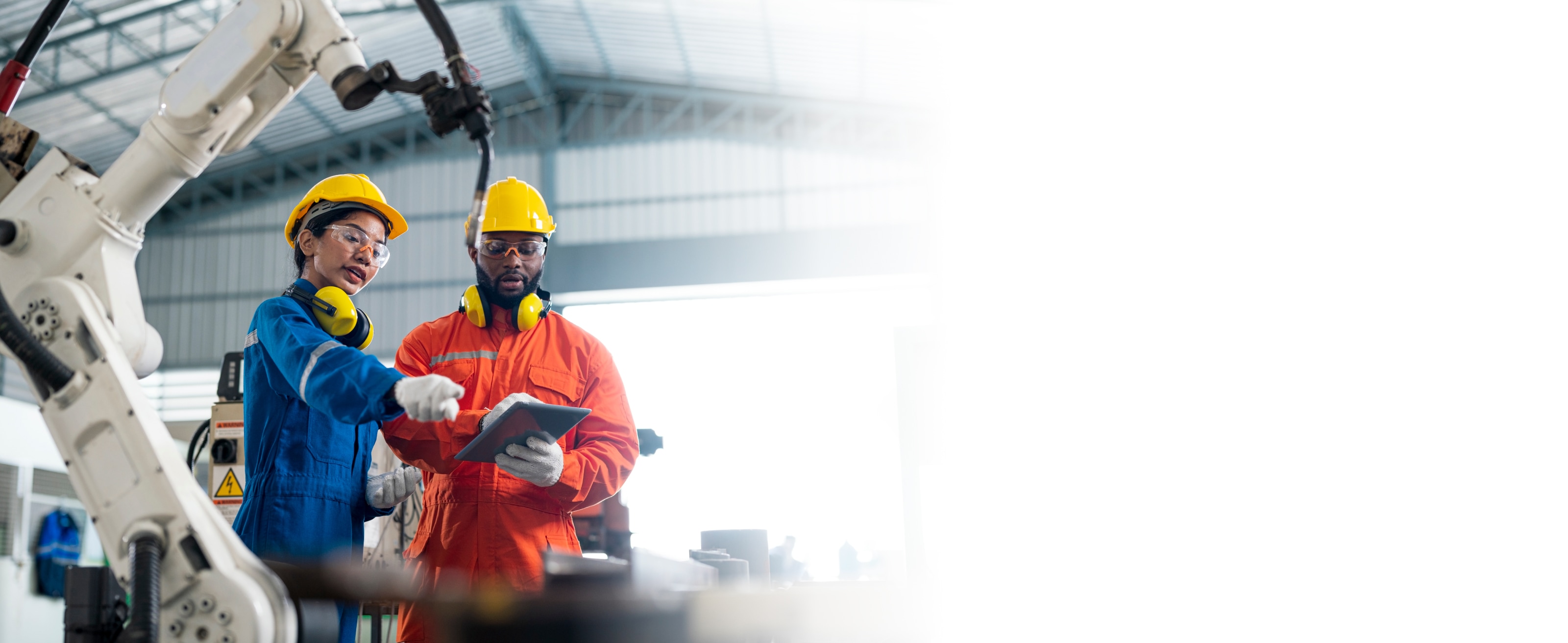 Manufacturing robot arm and two manufacturing workers looking at a tablet. 