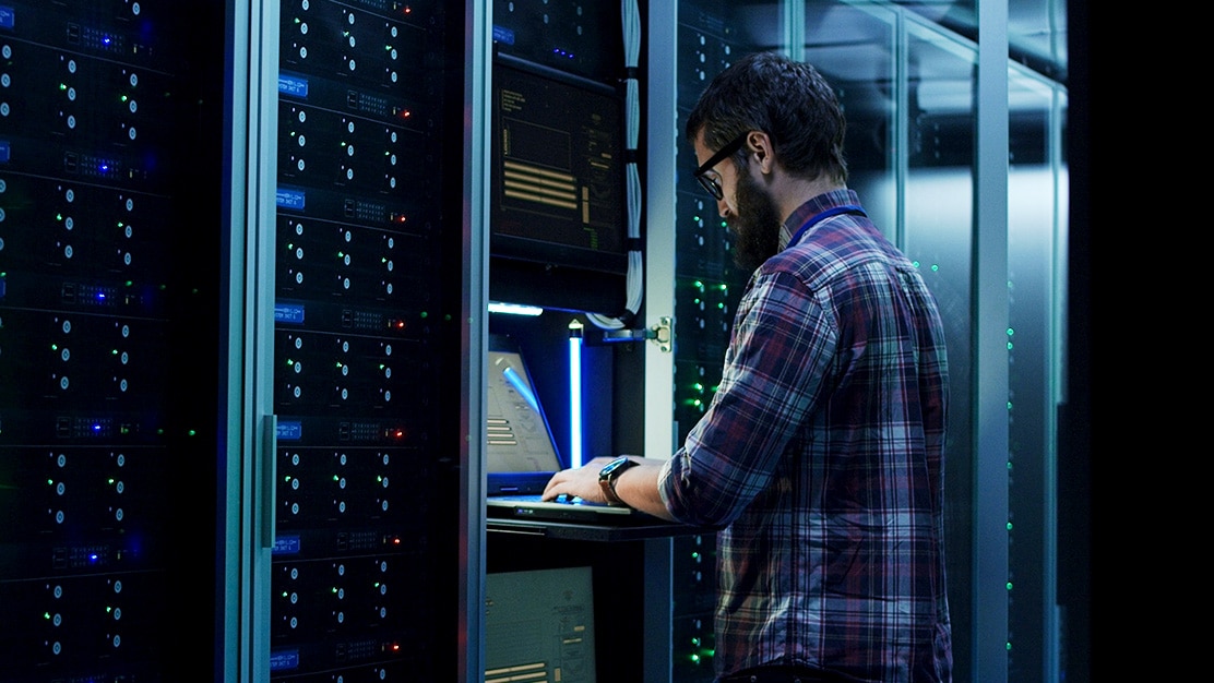 An employee at a workstation in a data center typing on a laptop. 