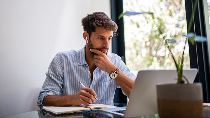 Person looking at a laptop screen and holding a pen